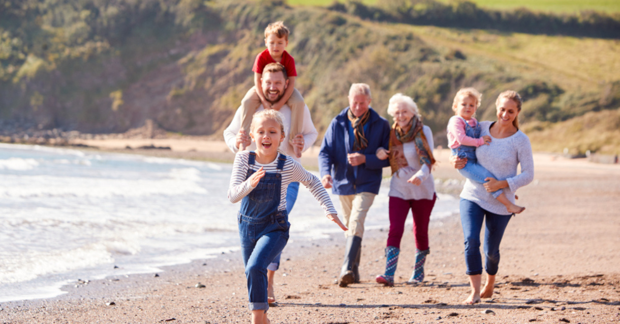 Multigenerational family running through beach